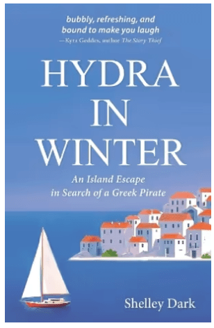 Book cover for Hydra in Winter by Shelley Dark. Blue Sky, blue sea, quintessential whitewashed buildings with terracotta rooves, sailing boat going past.