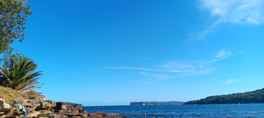 A bright blue sky with a kint of clouds, a deeper blue sea, two headlands on either side of the photograph.